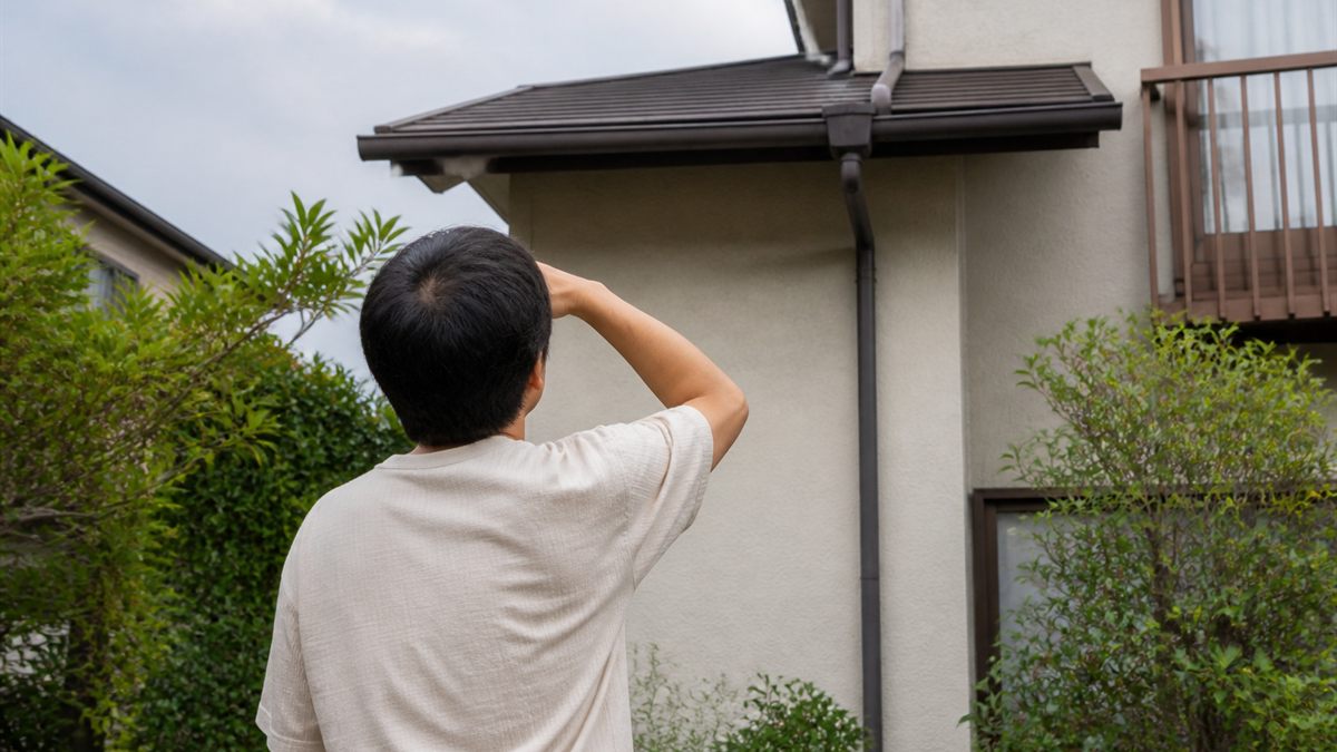 地上から自宅の屋根を見上げる人