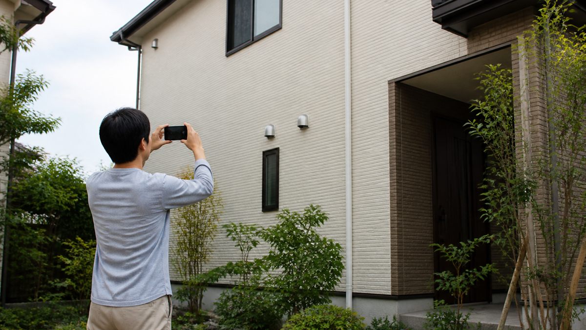 住宅の外壁を見上げる人