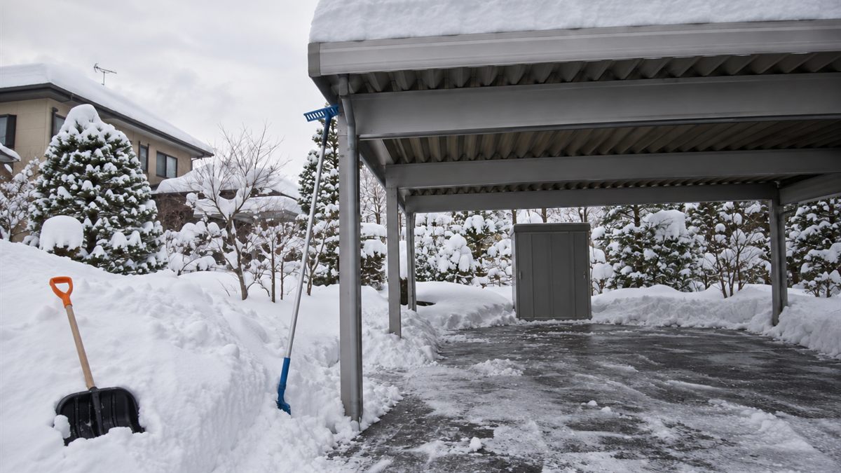 地上から見上げたカーポートの積雪と柄の長い雪下ろし道具