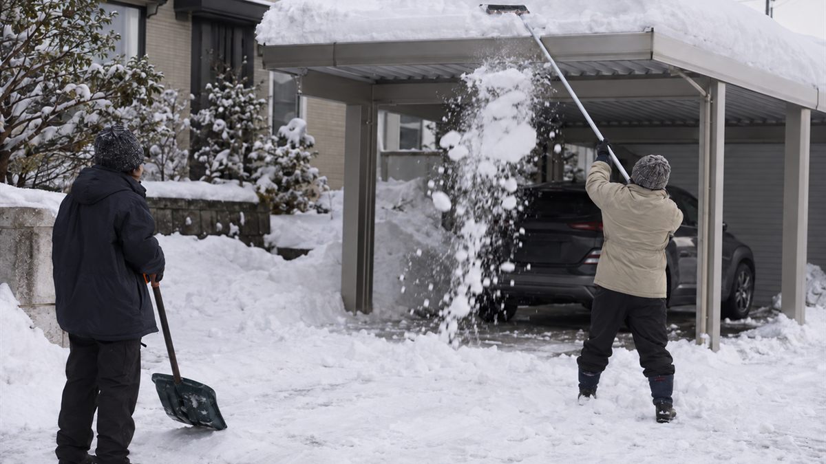 地上から柄の長い道具でカーポートの雪を下ろす2人