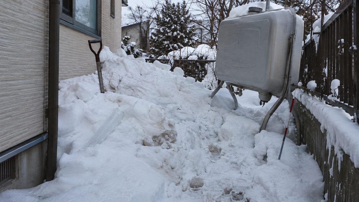 屋根から落ちた雪が積もった脇に立つ灯油タンク