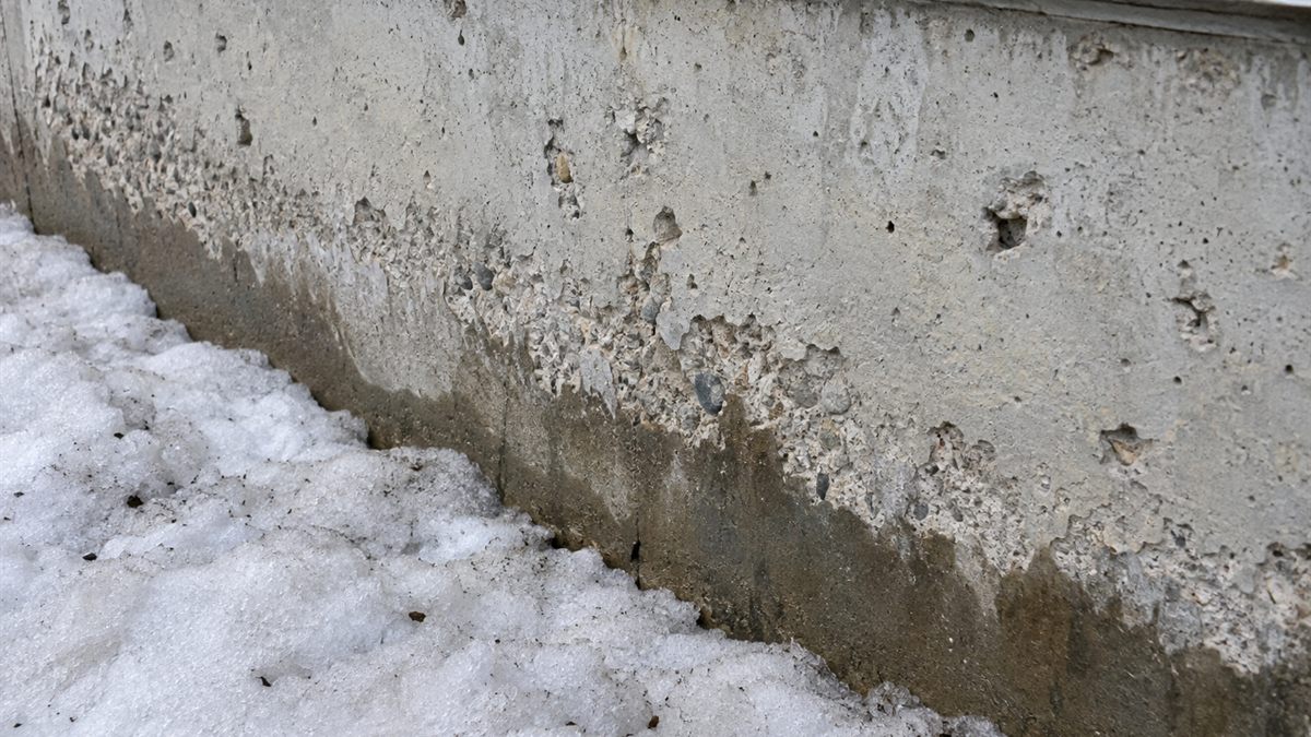 雪が残る打ちっぱなしの壁の足元で表面がはがれた部分