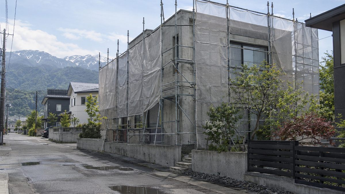 足場とメッシュシートに囲まれた打ちっぱなしの住宅